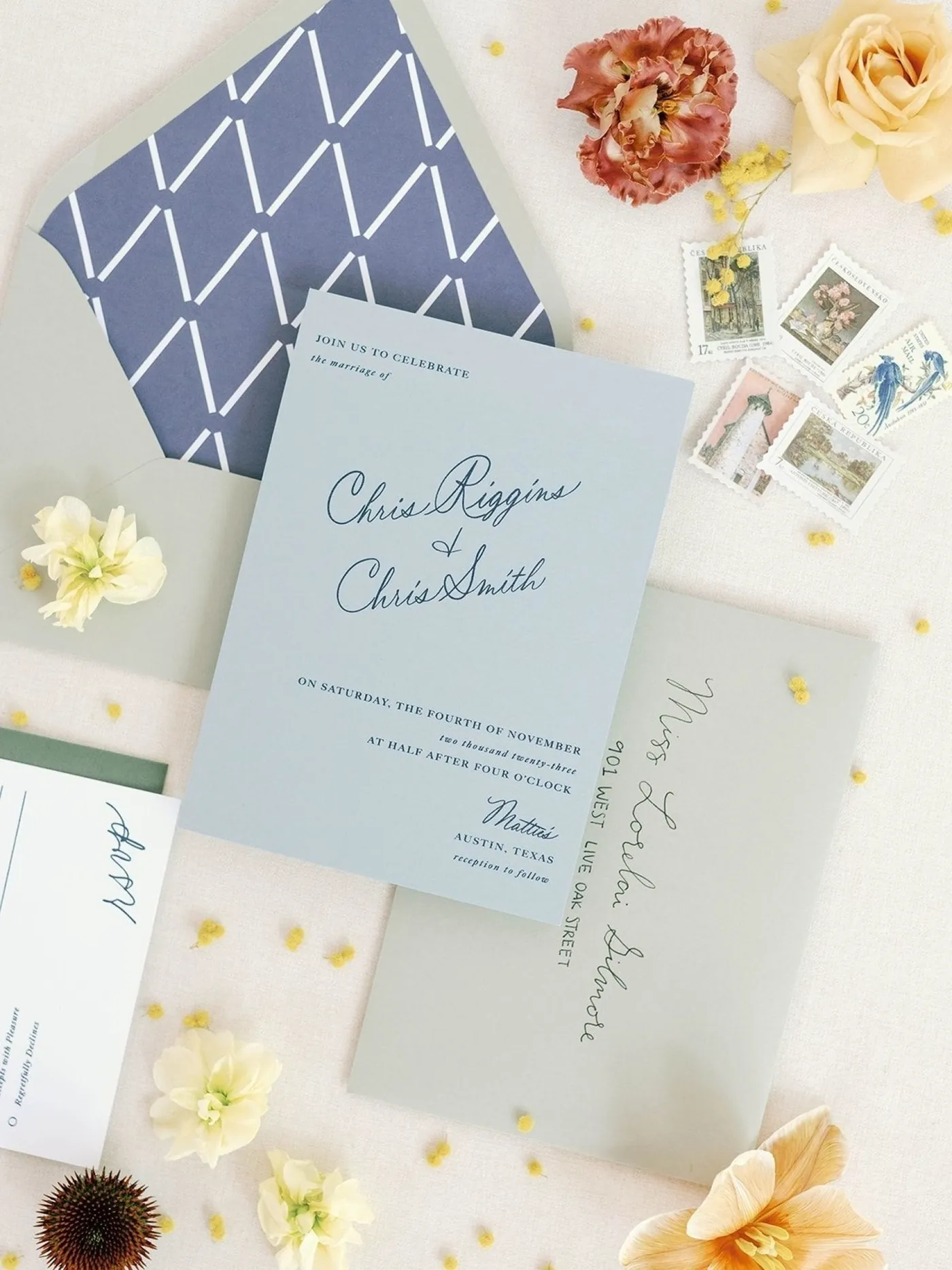Dusty blue invitation suite with a geometric envelope liner, vintage stamps, and soft yellow blooms