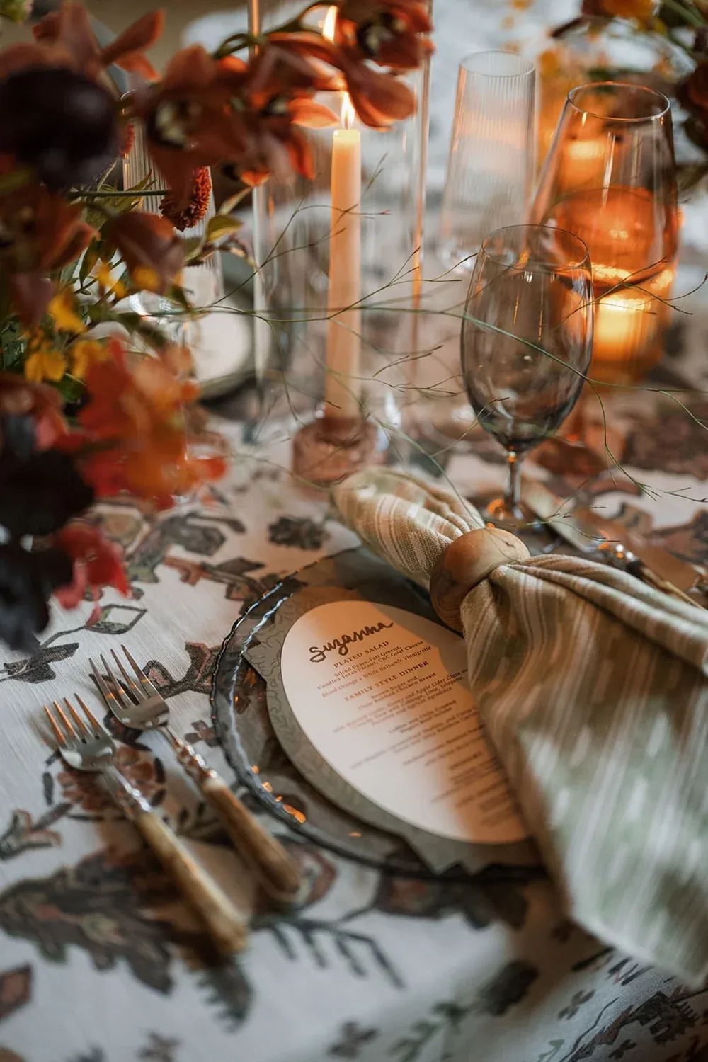 Round custom menu with a place card on a patterned tablescape lit by candles
