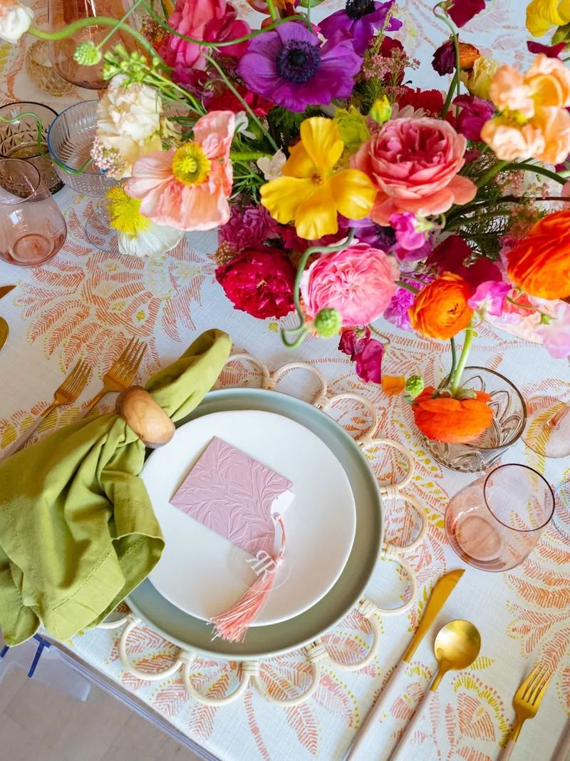 Pink embossed place card with a tassel on a place setting surrounded by vibrant florals